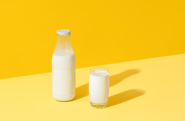 Milk in glass and bottle, minimalist on yellow background