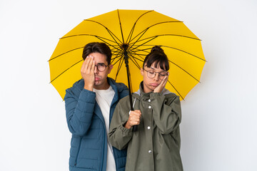 Young mixed race couple holding an umbrella isolated on white background with surprise and shocked...