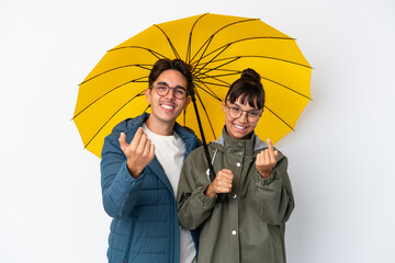 Young mixed race couple holding an umbrella isolated on white background inviting to come with hand. Happy that you came