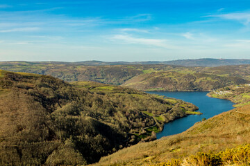 Fototapeta premium Blue water lake surrounded by autumnal forest and green meadows on a sunny day and blue sky. Chandrexa de Queixa reservoir. Ourense. Galicia