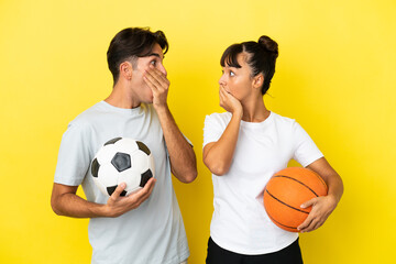 young sport couple playing football and basketball isolated on yellow background covering mouth...
