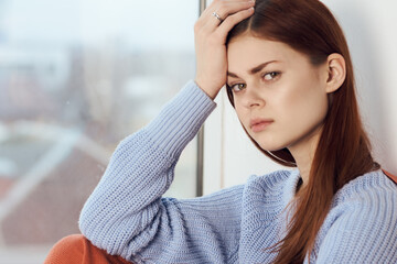 woman with sad expression sits by the window with a plaid