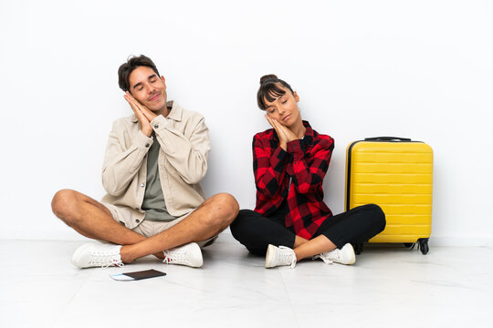 Young mixed race travelers couple sitting on the floor isolated on white background making sleep gesture in dorable expression