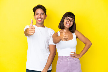Young mixed race couple isolated on yellow background giving a thumbs up gesture because something good has happened