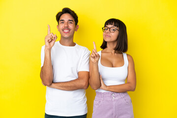 Young mixed race couple isolated on yellow background showing and lifting a finger in sign of the best