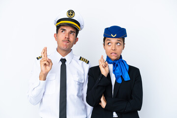 Airplane pilot and mixed race air hostess isolated on white background with fingers crossing and wishing the best