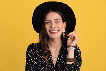 attractive woman posing isolated on yellow background wearing black hat and dress