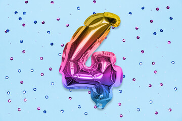 Rainbow foil balloon number, digit four on a blue background with sequins. Birthday greeting card with inscription 4. Top view. Numerical digit. Celebration event, template.