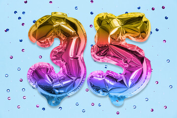 Rainbow foil balloon number, digit thirty five on a blue background with sequins. Birthday greeting card with inscription 35. Anniversary concept. Numerical digit. Celebration event, template.