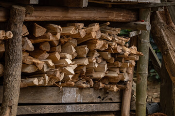A pile of stacked chopped firewood logs under a small wooden house. Chopped firewood used for cooking in an outdoor kitchen. 