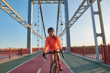 Smiling girl in sportswear ride bike on bridge