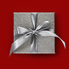gift silver glittering box with ribbon bow, isolated on red background, top view, useful for merry...