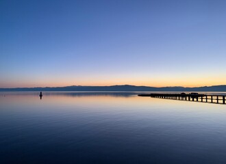 Silhouette of a long pier at the surface of the lake, sunset time, natural colors