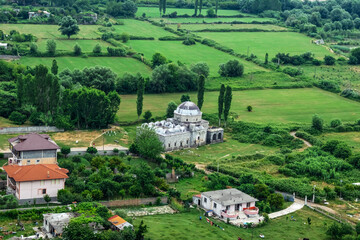 Fototapeta na wymiar Lead Mosque without minarets among green fields in a valley near Shkoder (Albania) - top view. Beautiful landscape with dilapidated Muslim temple in the countryside