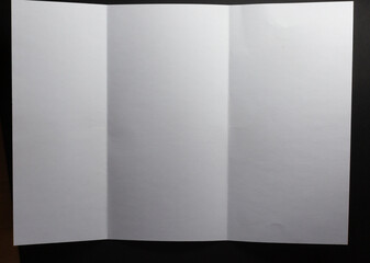 Light and shadow on creases in sheet of white paper folded into three sections, on black