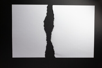 Two vertical sheets of white paper with torn edges facing, on black background
