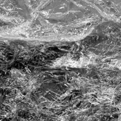 Reflecting light and shadow on creases and folds in scrunched clear plastic foil on dark background