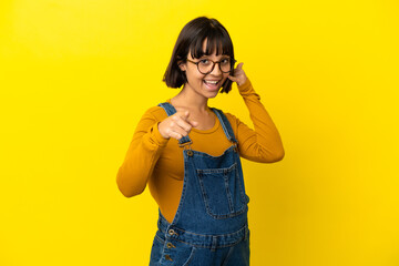 Young pregnant woman over isolated yellow background making phone gesture and pointing front