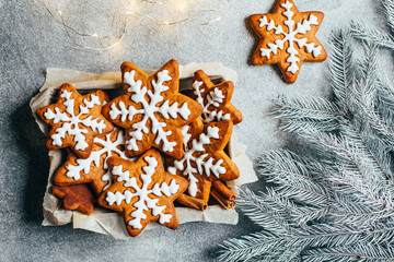 top view of christmas gingerbread cookies in the form of snowflakes with icing next to branches of...