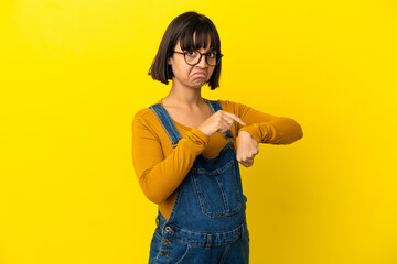 Young pregnant woman over isolated yellow background making the gesture of being late