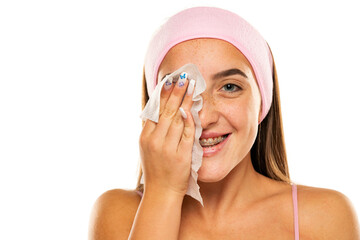 young happy woman with headband cleans her face with wet wipes