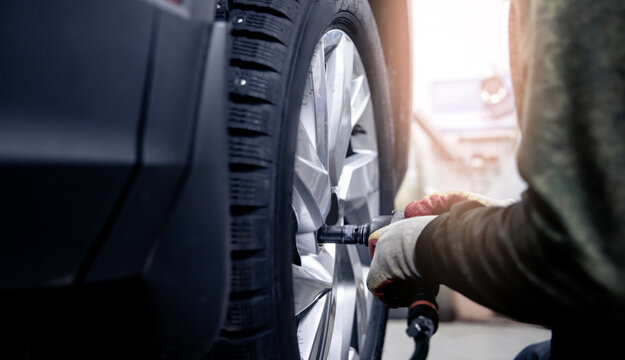 Concept Replacement of winter and summer tires. Mechanic unscrew wheels from car with light