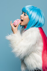 Young asian pop art woman holding delicious donut near open mouth isolated on blue
