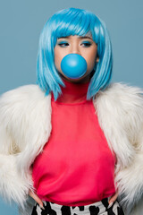 Asian woman in furry jacket blowing bubble gum isolated on blue