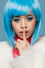 Portrait of asian pop art model in furry jacket showing shh gesture isolated on blue