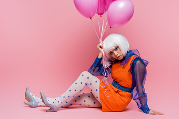 Pretty asian woman in pop art clothes holding balloons on pink background