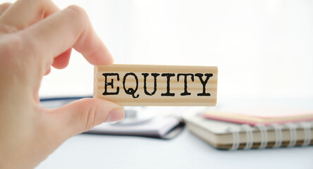 Wooden blocks with the text: equity. The text is written in black letters and is reflected in the mirror surface of the table. EQUITY - securities that represent ownership