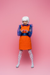 KYIV, UKRAINE - DECEMBER 10, 2020: Smiling asian pop art model holding joystick on pink background
