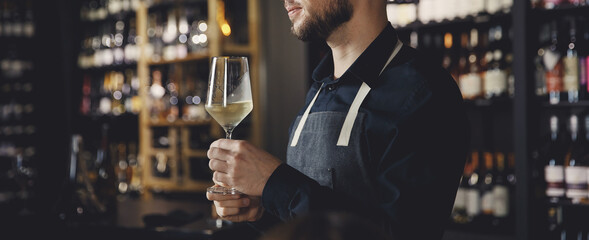 Banner sommelier man holds glass with white wine in restaurant, tests aroma and color