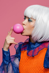 Asian woman in white wig blowing bubble gum isolated on pink