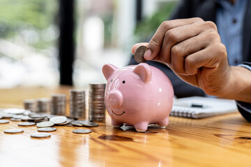 A businessman holding a coin in a piggy bank. Placing coins in a row from low to high is comparable to saving money to grow more. The concept of growing savings and saving by investing in stock funds.