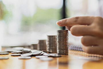 Business Woman putting a coin on a pile of coins. Placing coins in a row from low to high is comparable to saving money to grow more. The concept of growing savings and saving by investing in stock