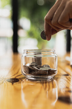 Close-up of a man putting a coin in a glass jar with a bunch of coins inside, he is a stock fund investor and stock investor. Savings ideas to invest in stocks and funds.