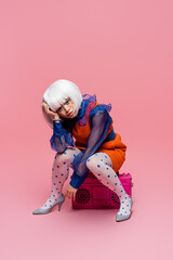 Stylish asian pop art model sitting on boombox on pink background