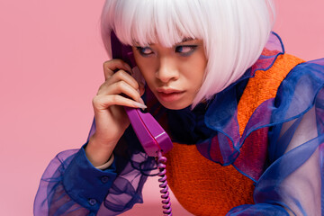 Asian pop art model talking on retro telephone with cable on pink background