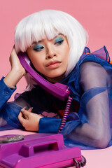 Stylish asian pop art model talking on blurred vintage telephone on pink background