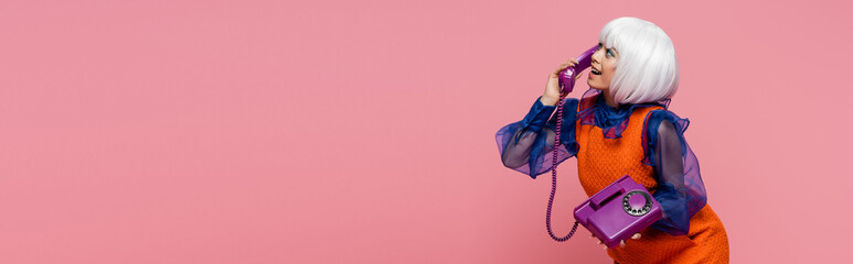 Side view of cheerful asian pop art model talking on telephone isolated on pink, banner