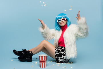 Smiling asian pop art woman in 3d glasses throwing popcorn on blue background