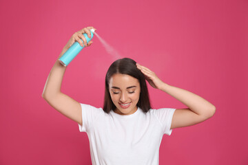 Young woman applying dry shampoo against pink background - obrazy, fototapety, plakaty