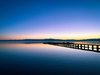 Fototapeta na wymiar Silhouette of a long pier at the surface of the lake, sunset time, natural colors