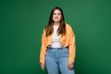 Cheerful plus size woman looking at camera isolated on green