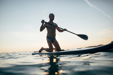 Senior man paddling board on sunset sea