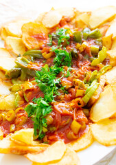 A close up shot of fried potato with tomato sauce and chopped parsley. Selective focus on middle area