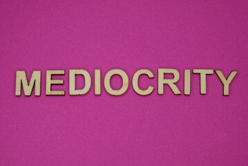  word mediocrity in small wooden letters on a pink background