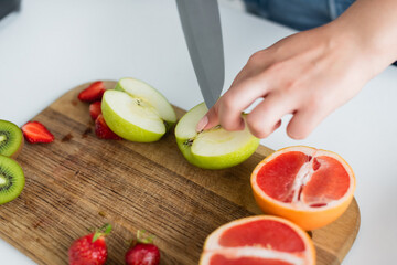 Cropped view of woman cutting apple near grapefruit and strawberries on cutting board