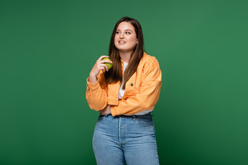 Smiling woman with overweight holding apple isolated on green